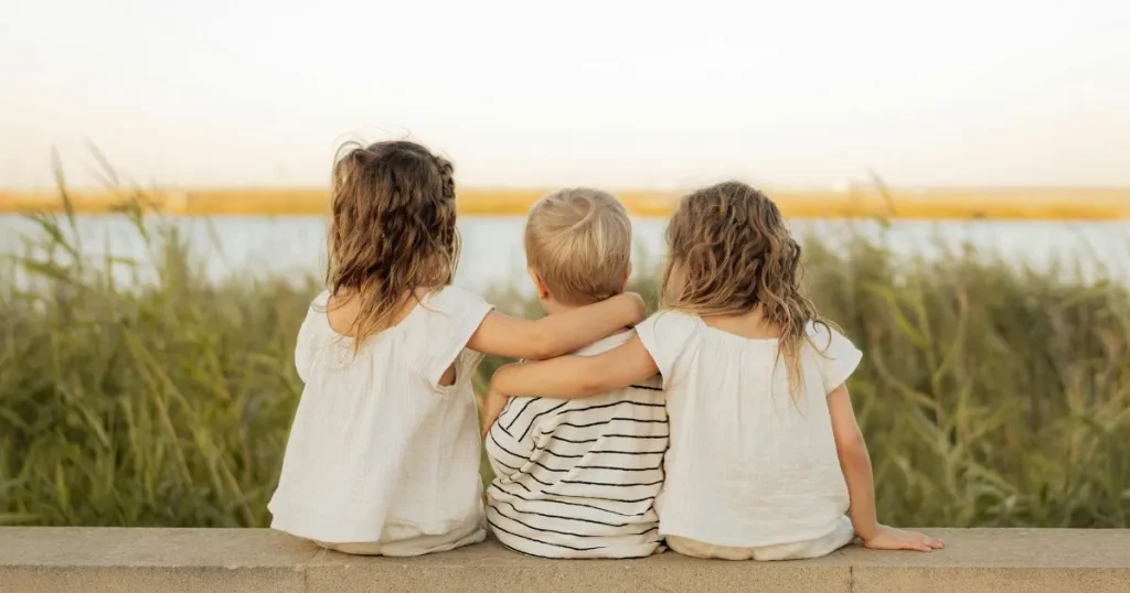 草原に並んで座る子どもたちの後ろ姿